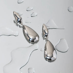Silver teardrop dangle earrings with a polished finish, surrounded by water droplets.