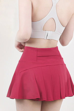 Red pleated skort with a high waist and flared hem, styled with a sports bra.