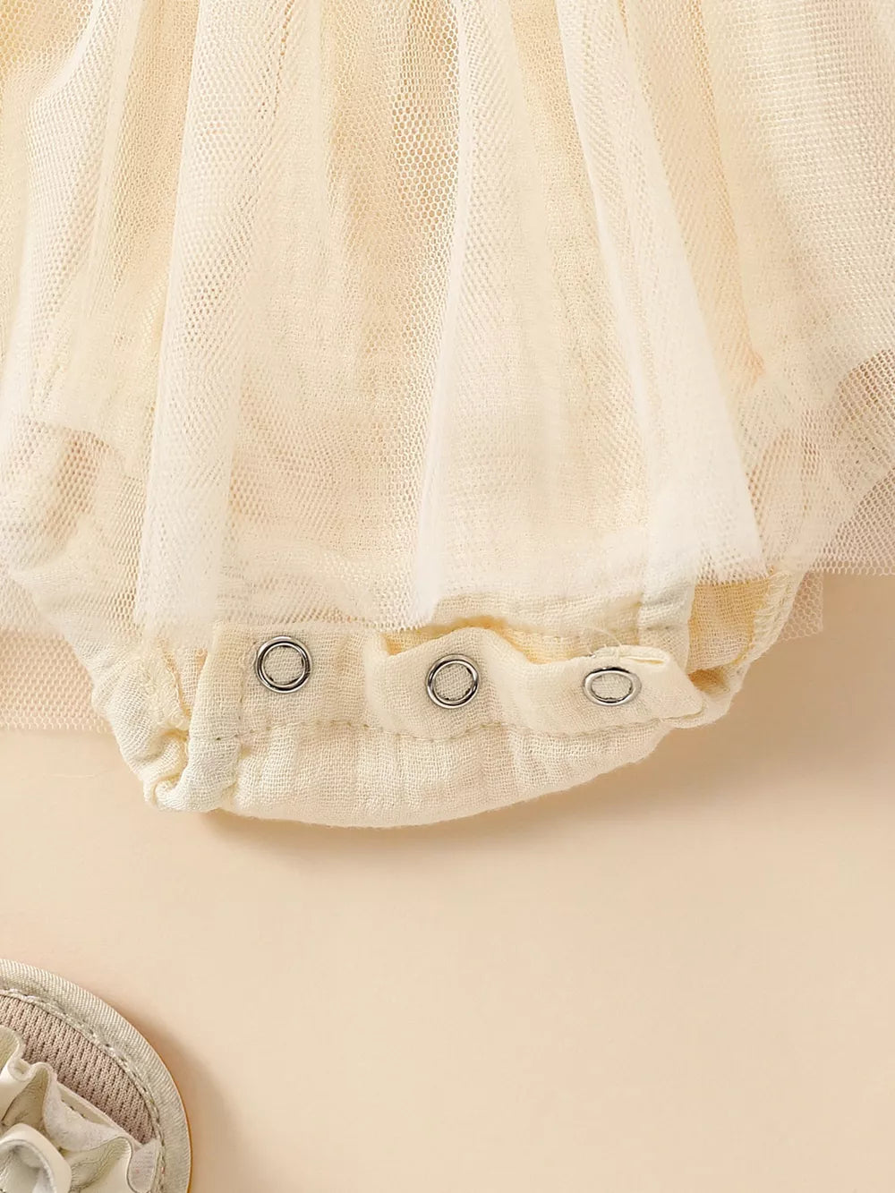 Apricot smocked baby bodysuit with snap closure and tulle overlay detail.