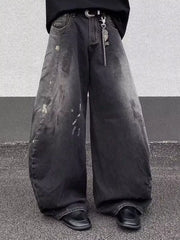 Men's black wide leg distressed jeans with paint splatters and a chain belt detail.