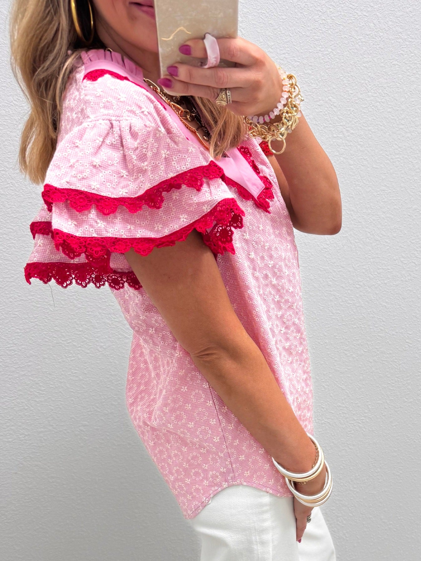 Pink eyelet embroidered blouse with flutter sleeves and red lace trim.