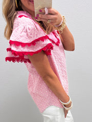 Pink eyelet embroidered blouse with flutter sleeves and red lace trim.