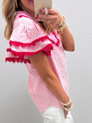 Pink eyelet embroidered blouse with flutter sleeves and red lace trim.