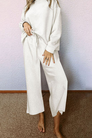 White loungewear set with textured geometric pattern, crew neck, drop sleeves, and wide-leg pants with drawstring waist.