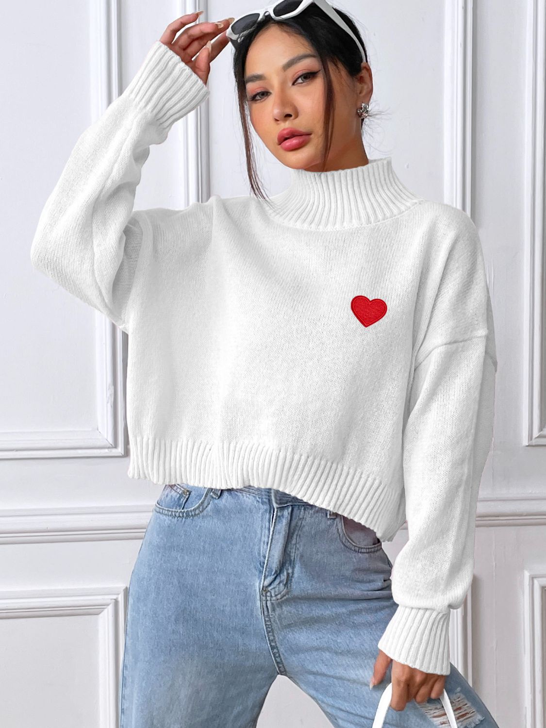 White cropped turtleneck knit sweater with embroidered red heart detail.