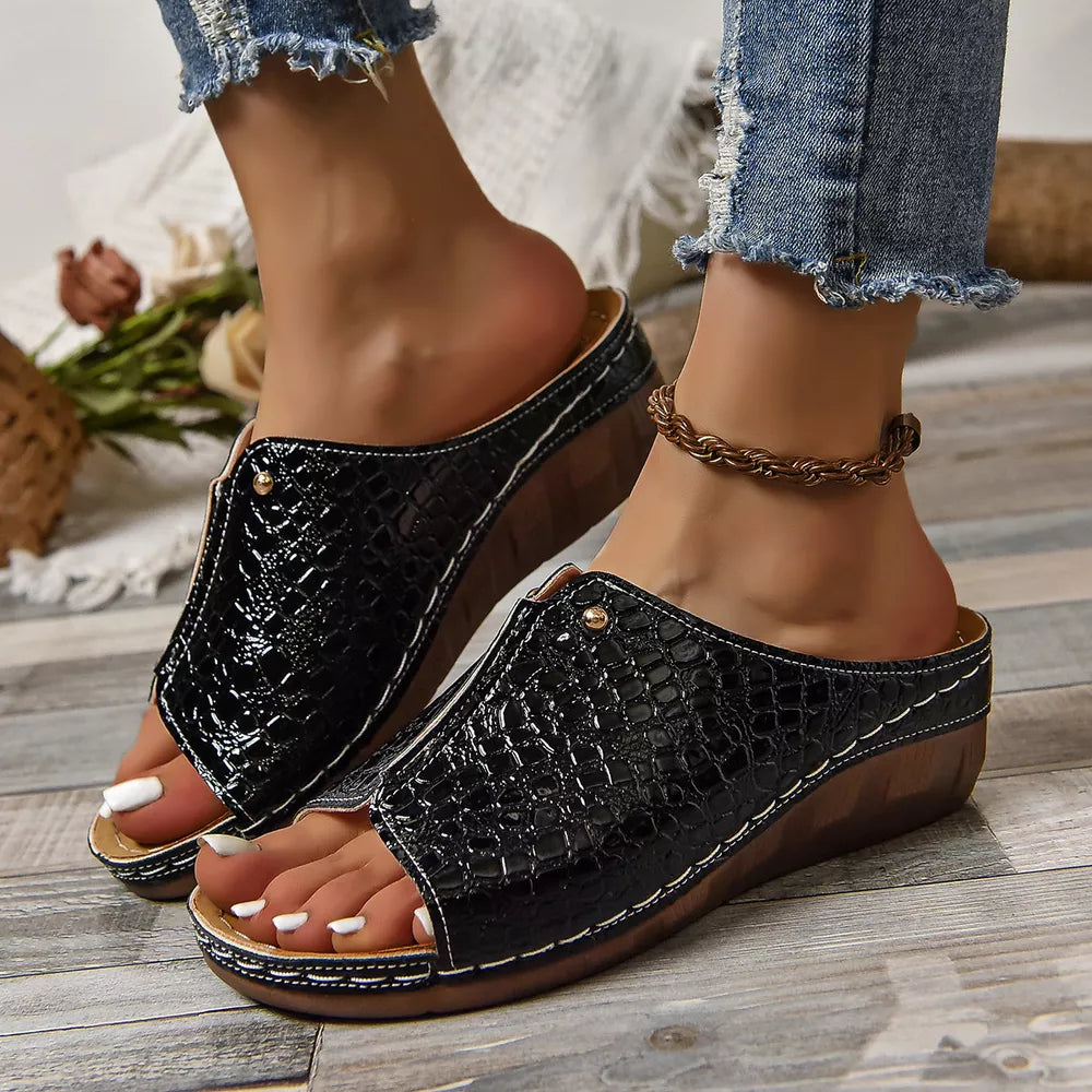 Black glossy crocodile-embossed wedge sandals with open toe and white stitching.
