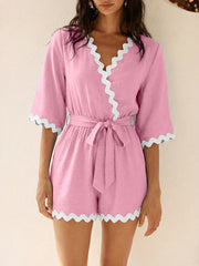 Pink maternity romper with 3/4 sleeves, V-neck, tie waist, and scalloped trim.