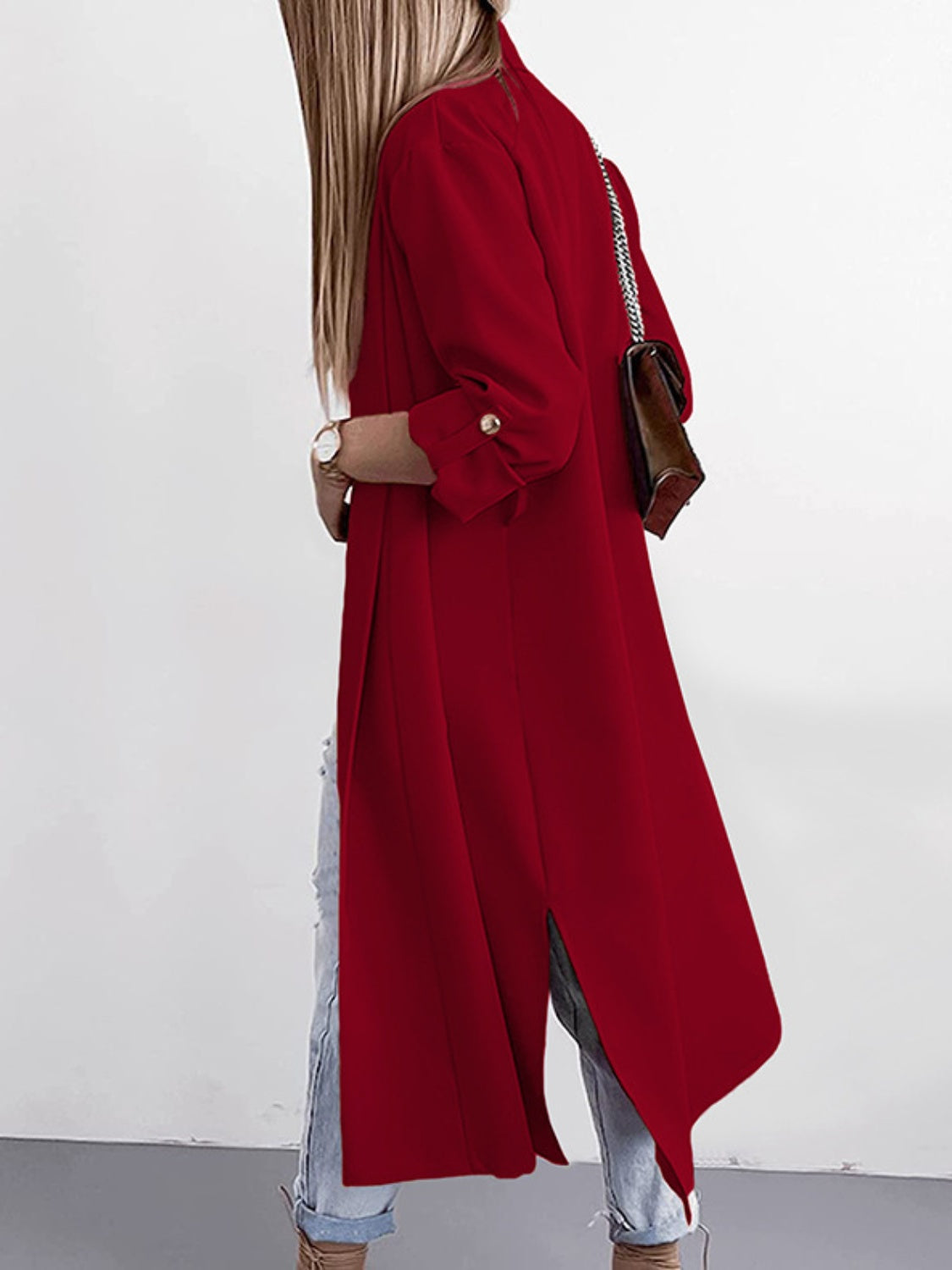 Deep red draped-front maxi coat with button cuffs and side slits, worn open over jeans.