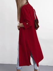 Deep red draped-front maxi coat with button cuffs and side slits, worn open over jeans.