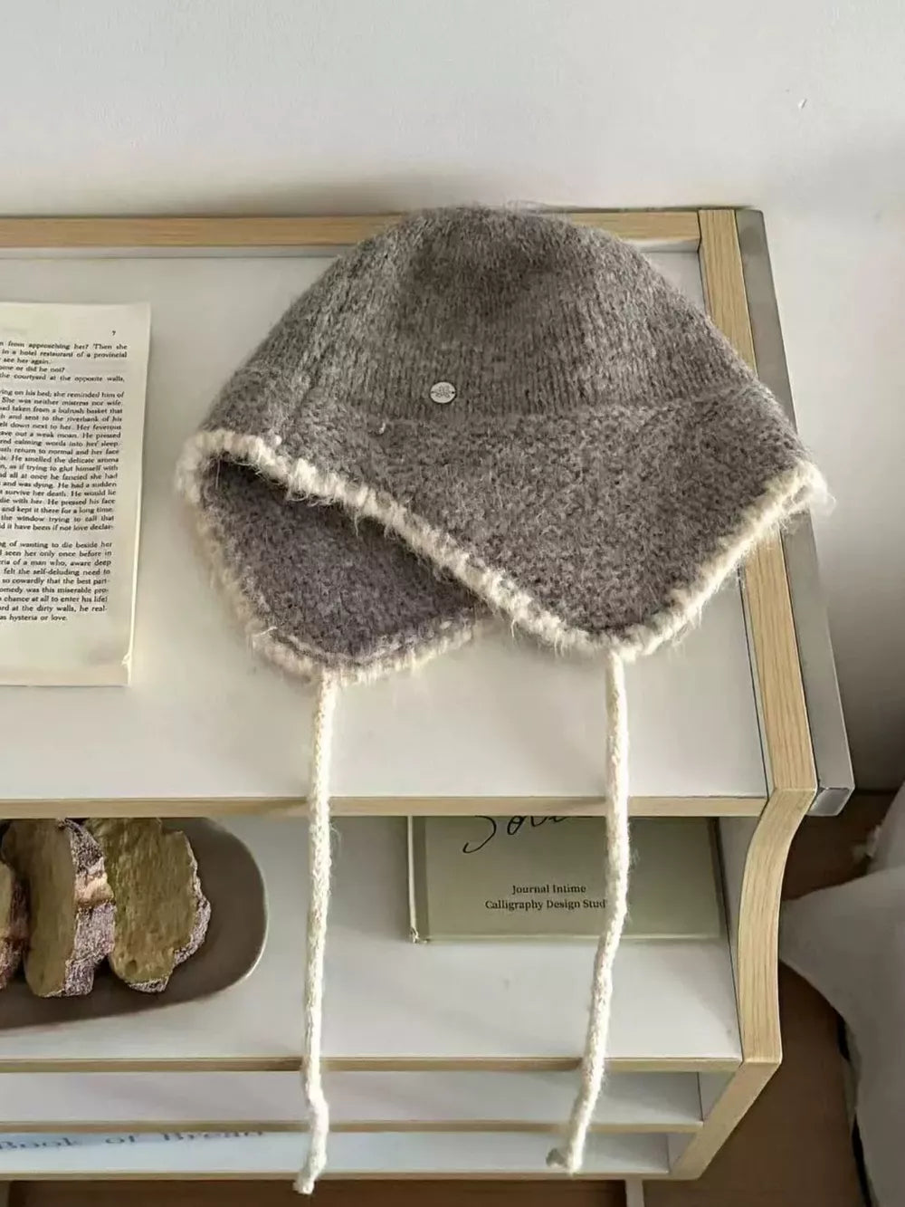 Gray wool-blend hat with ear flaps, braided ties, and contrast trim.