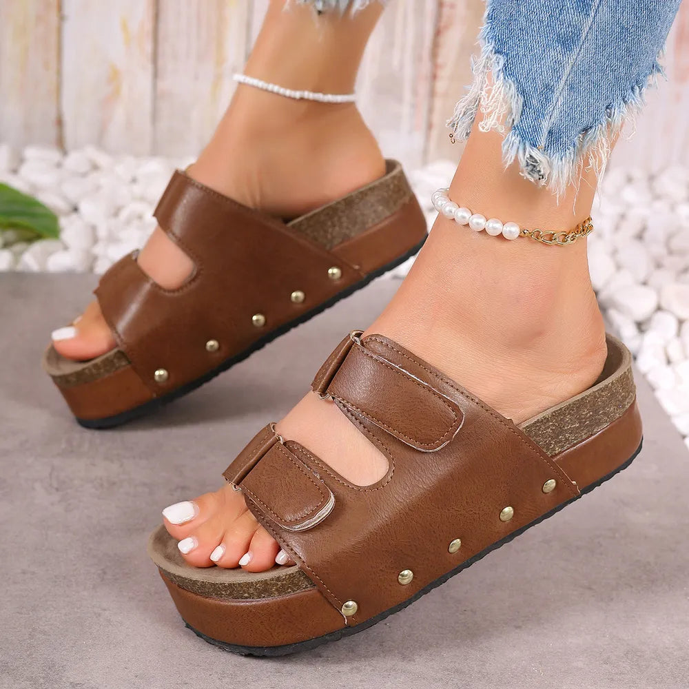 Brown platform sandals with double buckle straps and studded cork sole detail.