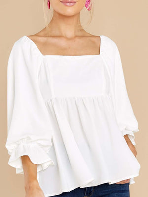 White babydoll blouse with square neckline, puff sleeves, and ruffled cuffs.