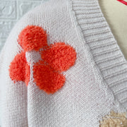 Ivory knit cardigan with textured orange floral embroidery detail.