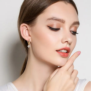 Gold huggie earrings with a small, sparkling clover charm.