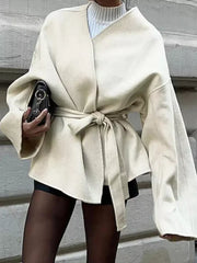 Beige belted trench coat with tie waist and dropped shoulders, styled with a black clutch.