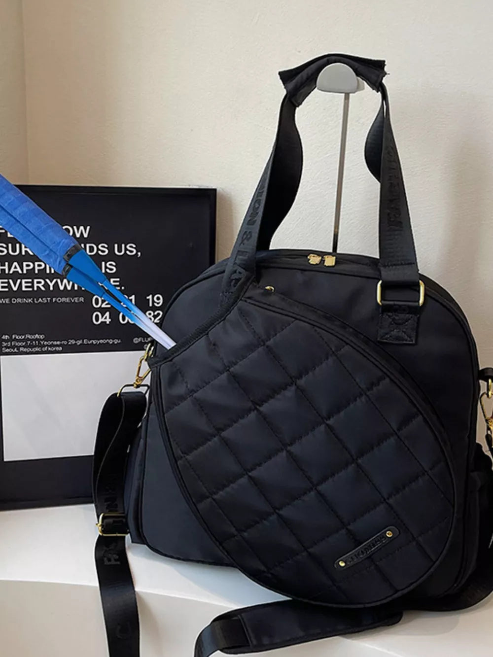 Black quilted Oxford bag with racket compartment and adjustable strap.