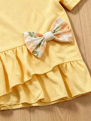 Light yellow cotton baby top with floral bow and tiered ruffles.