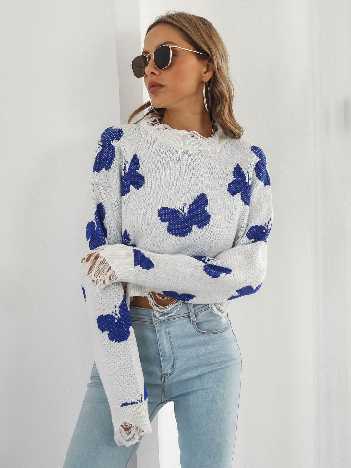 White cropped knit sweater with blue butterfly print and distressed details.