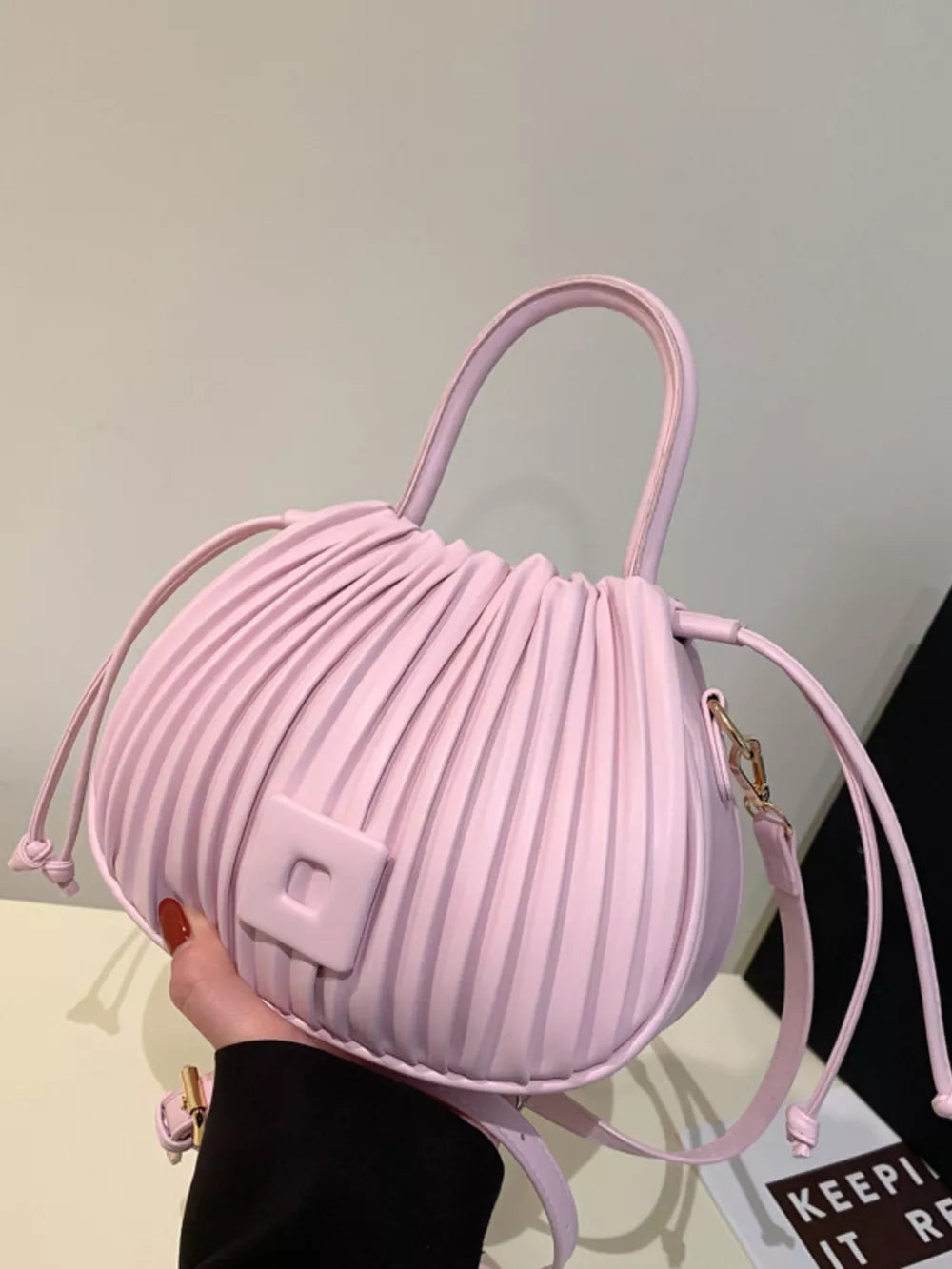 Pink pleated bucket bag with drawstring closure and square detail.