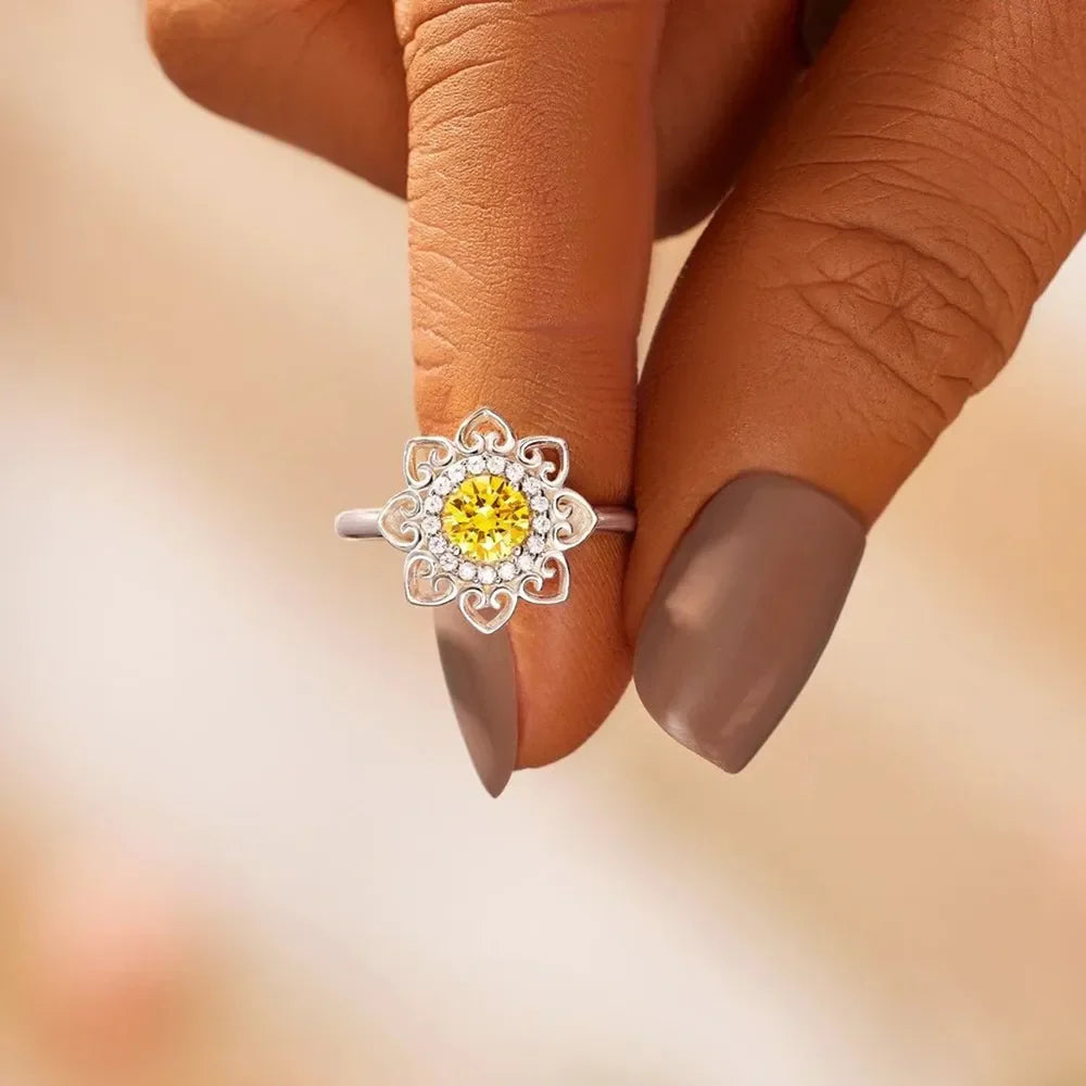Silver ring with yellow center stone and white accent stones in a floral filigree design.
