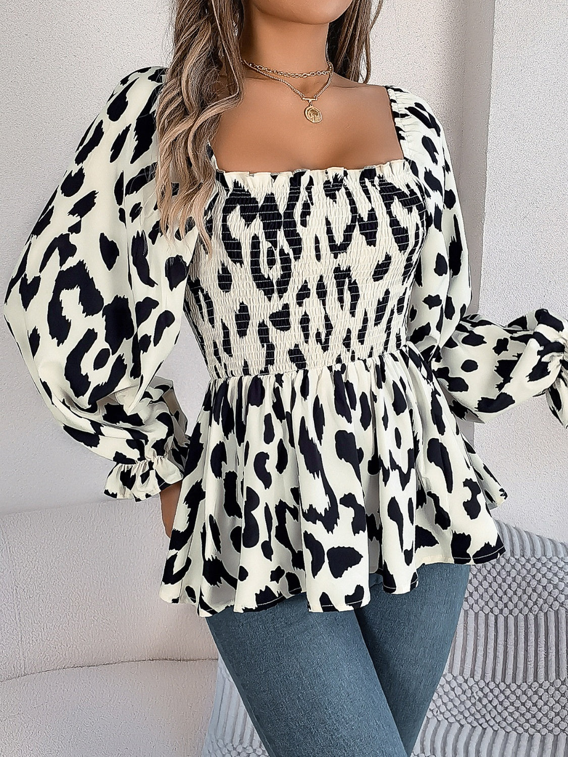 Smocked bodice square neck blouse in cream with black animal print, long puff sleeves, and peplum hem.