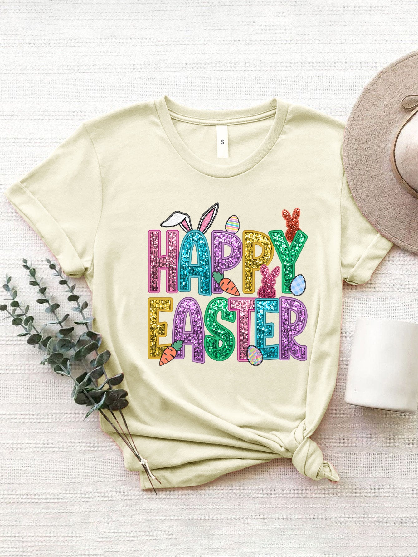 Cream t-shirt with glittery Happy Easter graphic featuring bunnies and carrots.