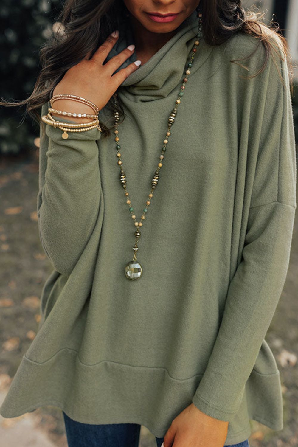 Army green tunic with cowl neck and drape front, styled with layered necklaces and bracelets.