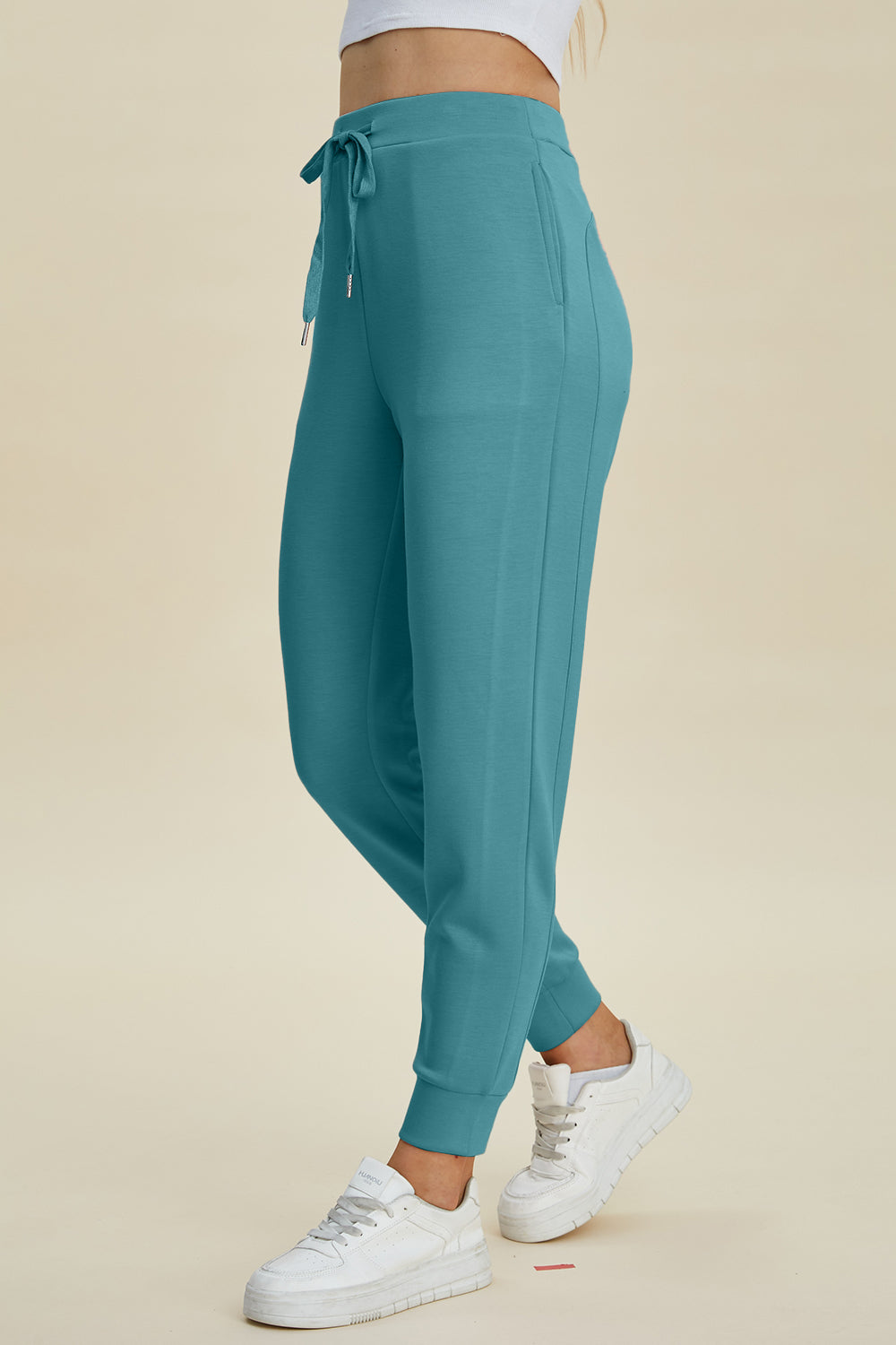 Teal joggers with drawstring waist and cuffed ankles, styled with white sneakers.