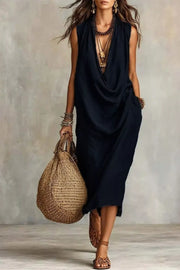 Black cowl neck midi dress with pockets, sleeveless, relaxed fit, worn with sandals and bag.