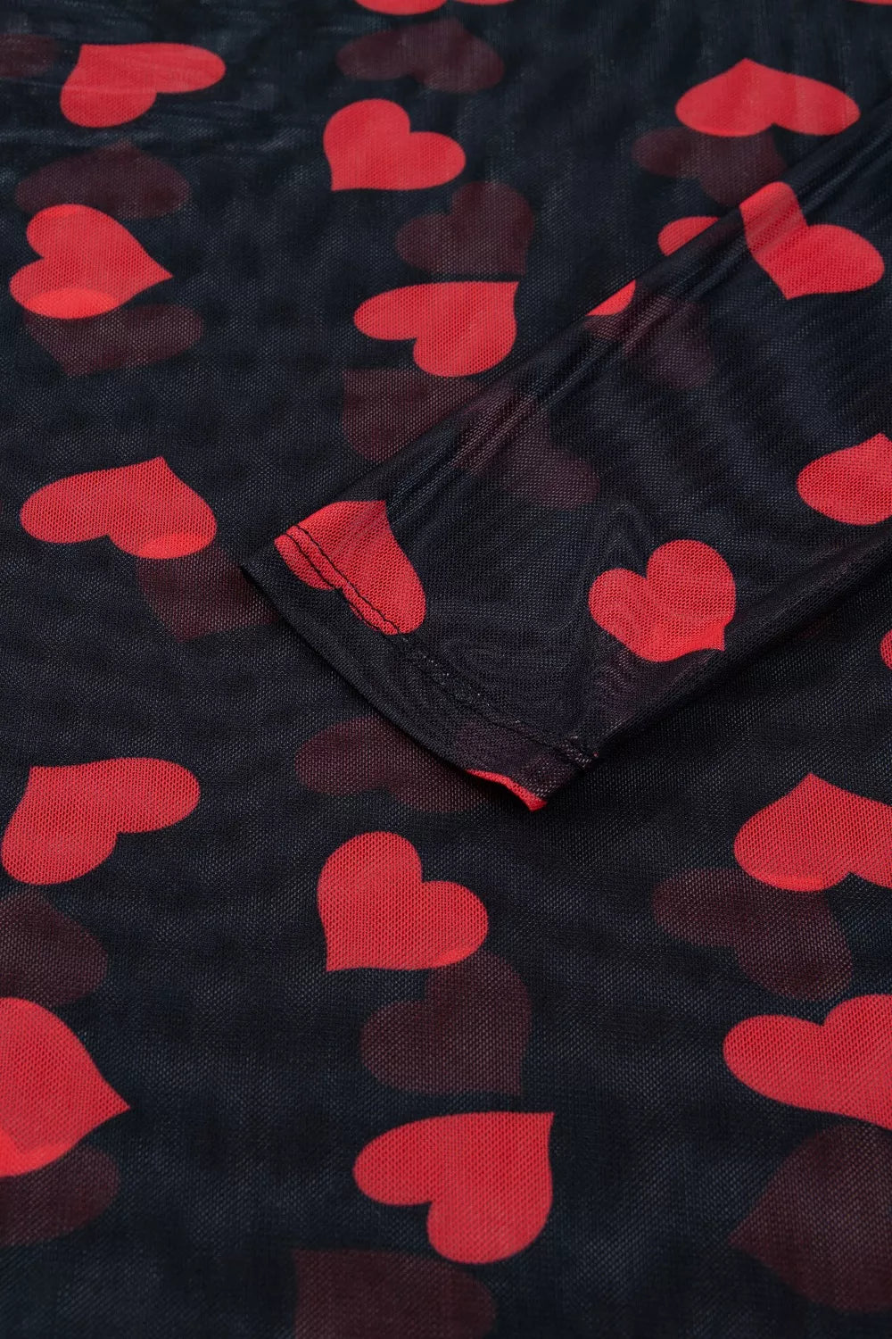 Sheer mesh blouse with red heart print and long sleeves.