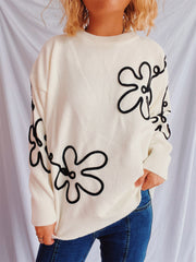 Beige knit sweater with black floral outline pattern, crew neck, long sleeves.