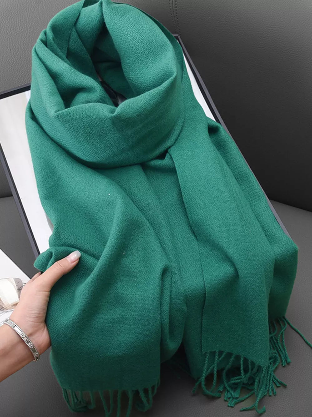 Green fringed scarf with a soft texture, styled loosely.