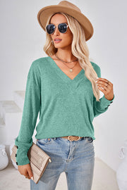 Green v-neck long sleeve top with button cuffs, styled casually.