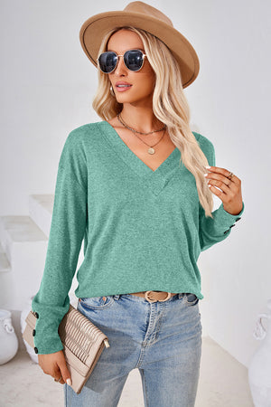 Green v-neck long sleeve top with button cuffs, styled casually.