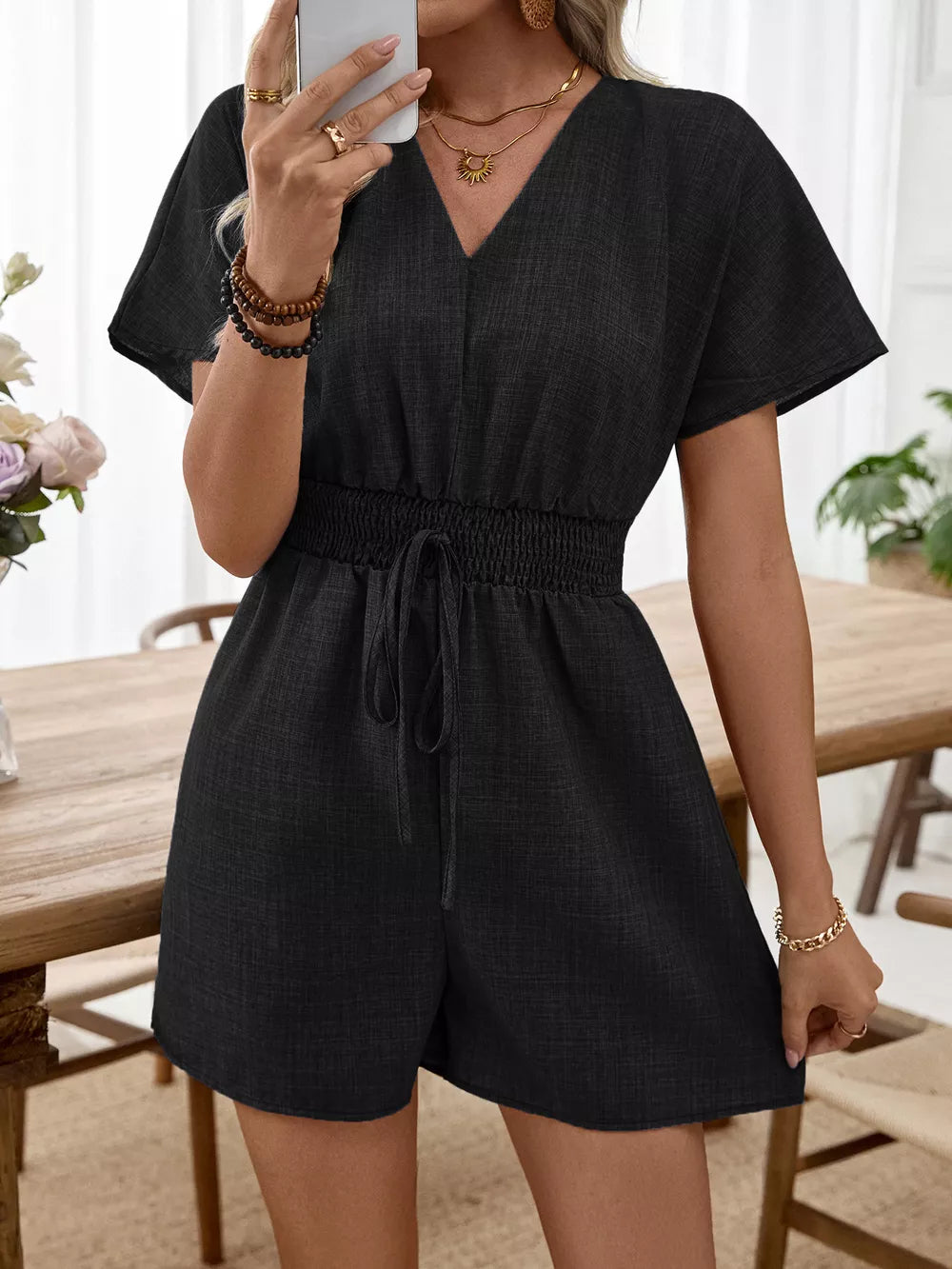 Black V-neck romper with flutter sleeves, smocked waist, and drawstring detail.