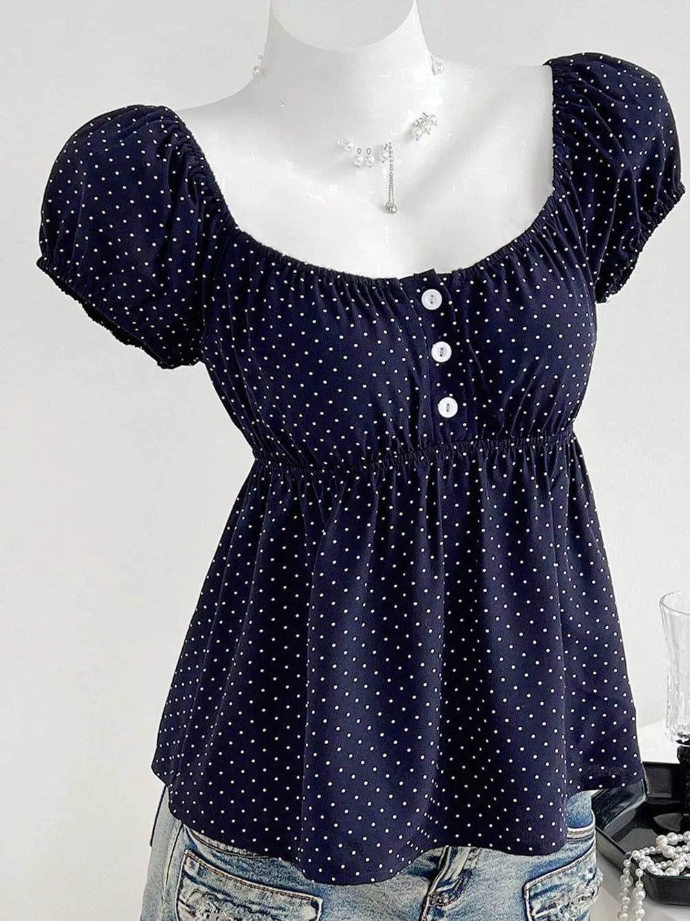 Navy polka dot puff sleeve shirt with square neckline and decorative buttons.