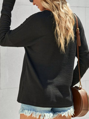 Black textured cotton henley shirt with long sleeves and button detail, styled with denim shorts.
