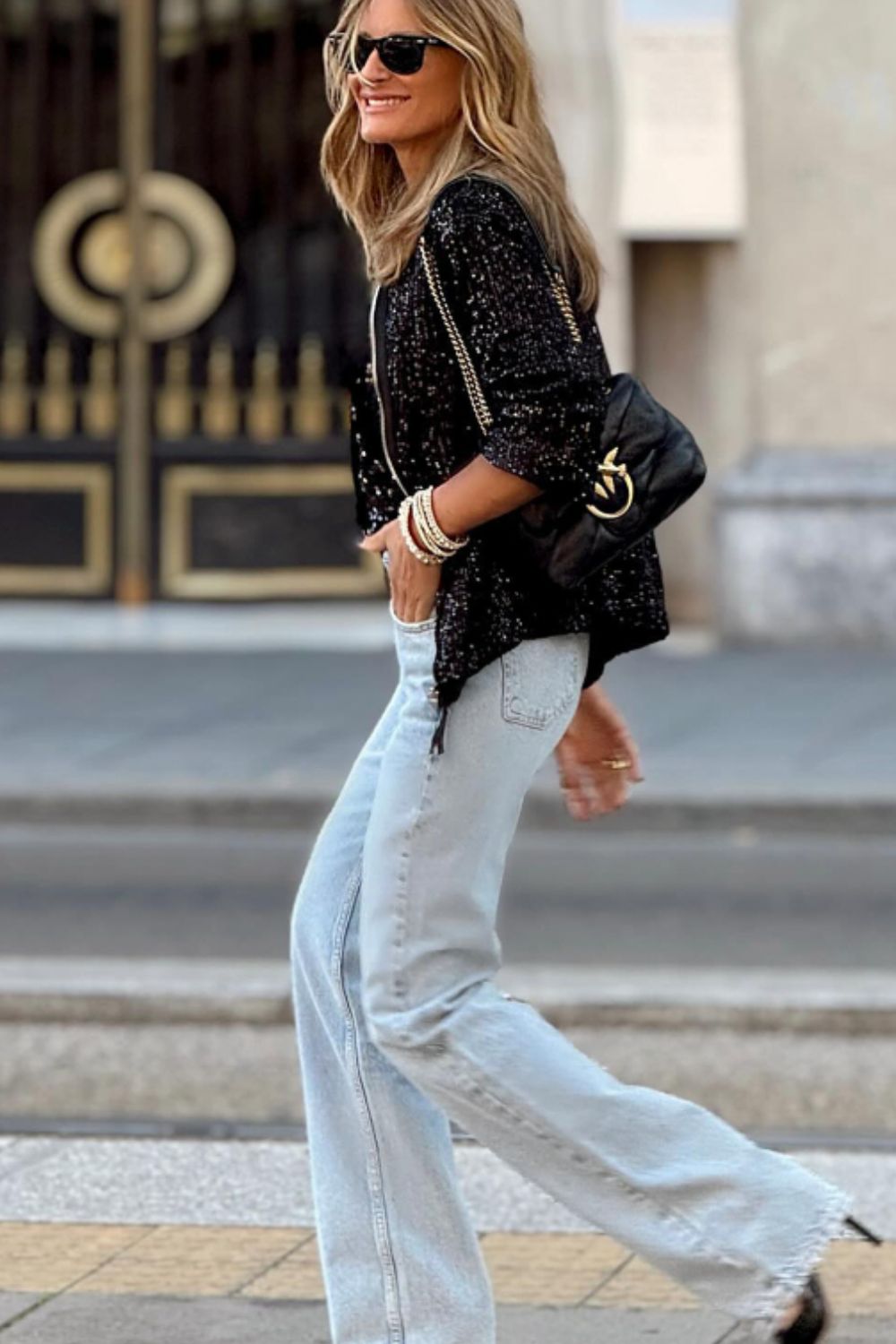 Black sequin bomber jacket with ribbed trim, worn by a woman with light wash jeans and a black handbag.