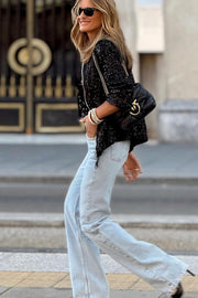 Black sequin bomber jacket with ribbed trim, worn by a woman with light wash jeans and a black handbag.