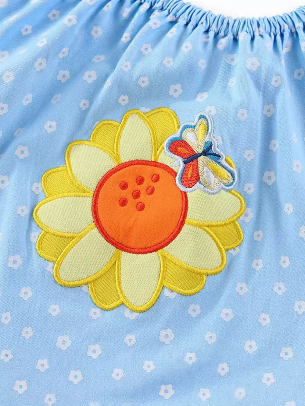 Baby dress with embroidered sunflower and butterfly detail on light blue floral print cotton fabric.