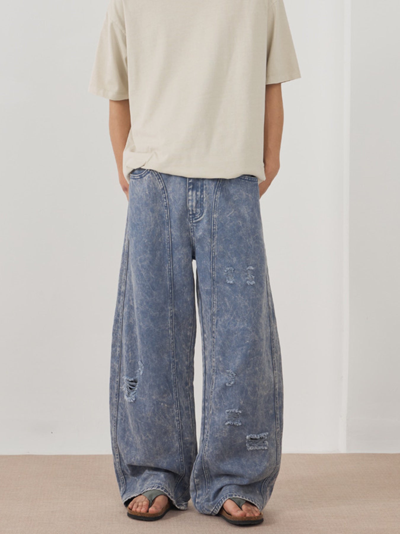 Men's blue acid wash distressed wide-leg denim jeans with ripped details.