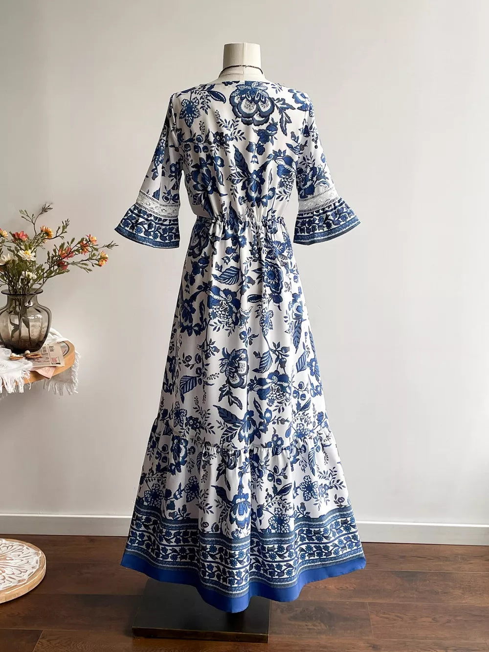 Maxi dress with blue floral print, V-neck, drawstring waist, tiered hem, and lace-trimmed bell sleeves.
