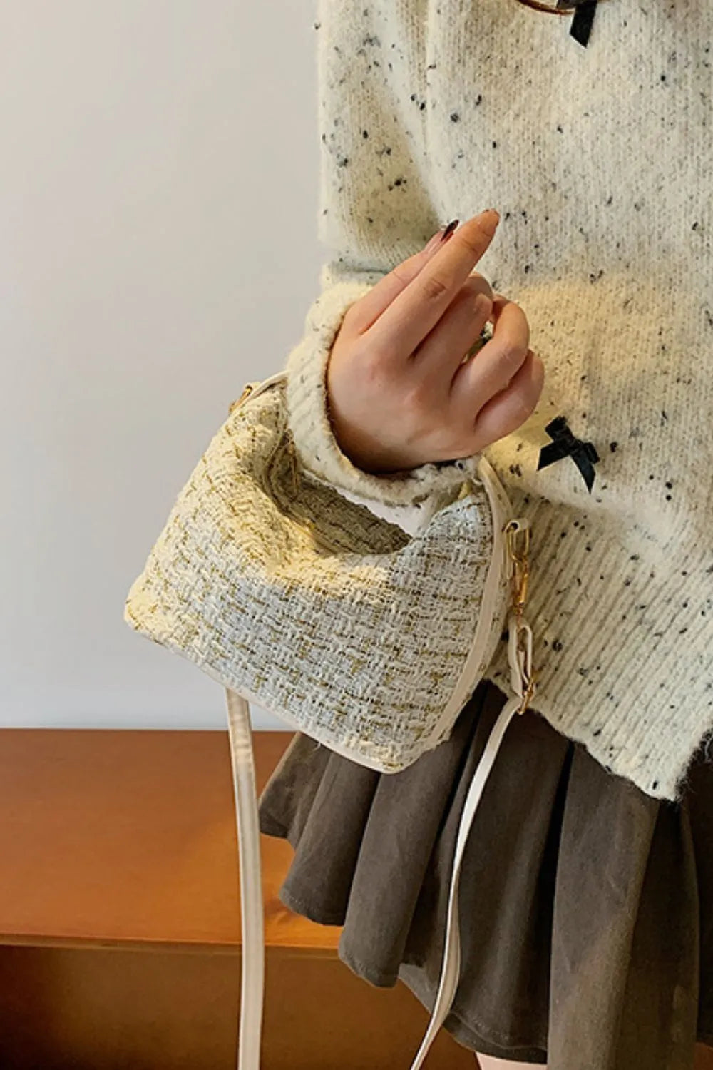 Tweed box bag with gold flecks and detachable strap, held by a hand.