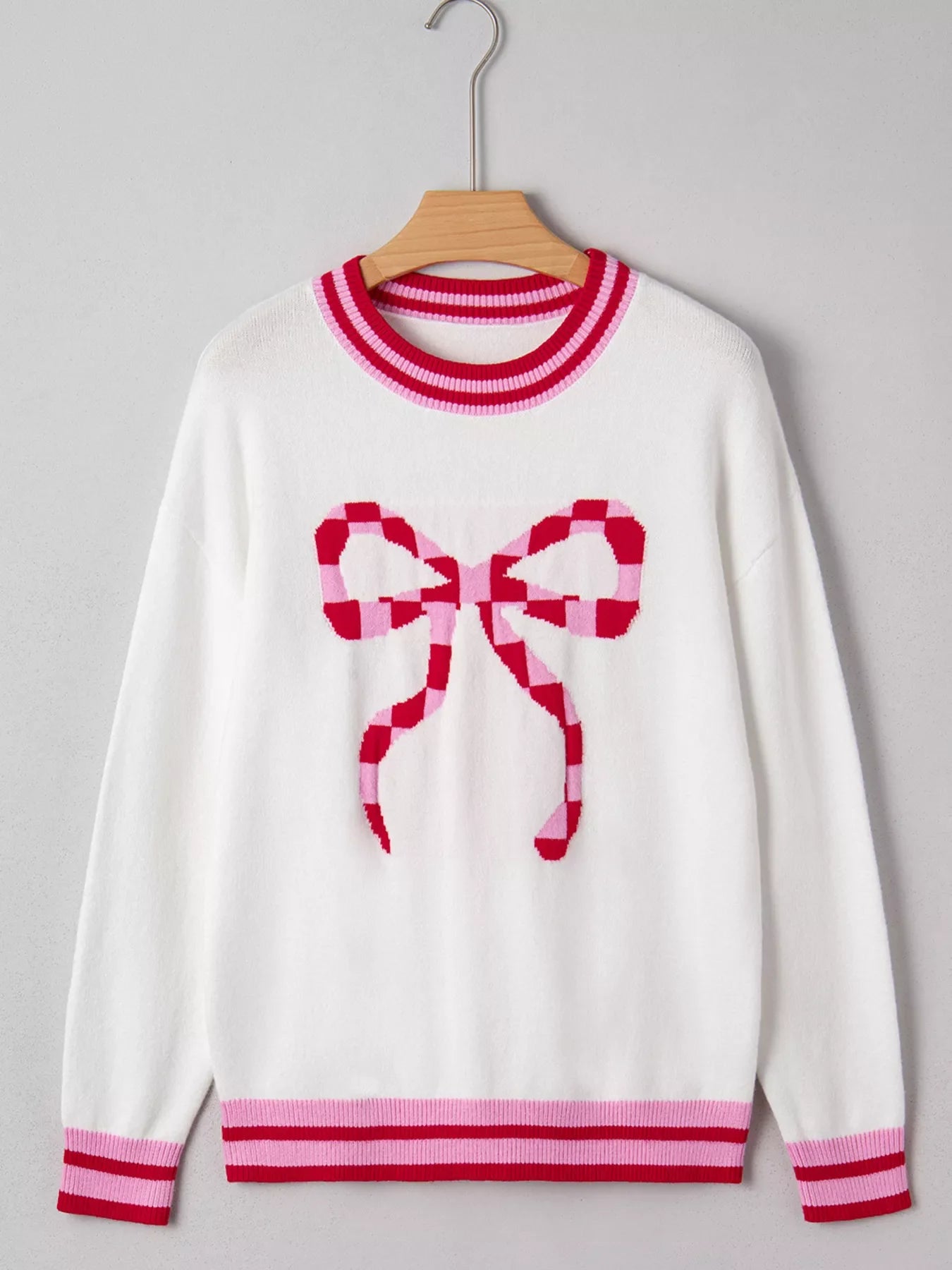 White round-neck sweater with a pink and red checkered bow graphic and striped cuffs and hem.