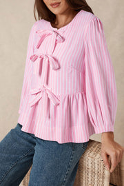 Blush pink striped peplum blouse with bow details and long sleeves.