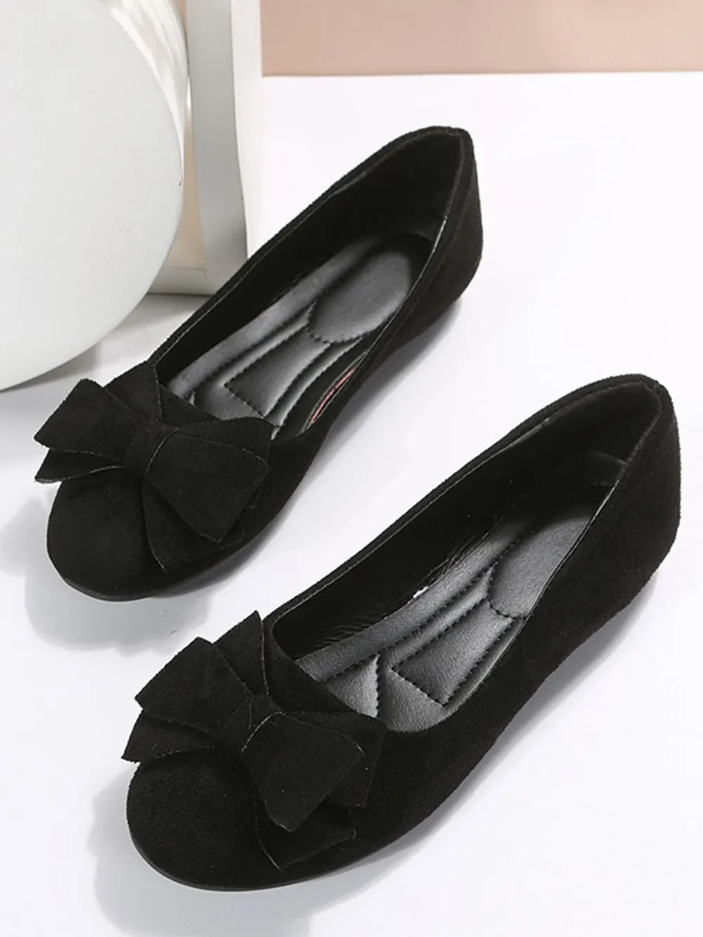 Black suede pointed-toe flats with bow embellishment and padded insole.