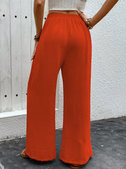 Orange-red textured palazzo trousers with dramatic slits and wide legs.