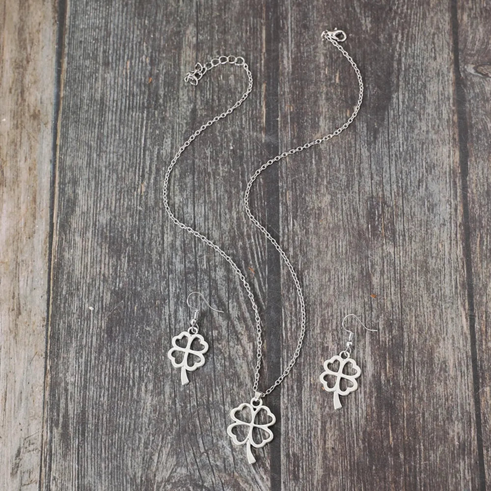 Silver four-leaf clover pendant necklace and matching earrings jewelry set on wood background.