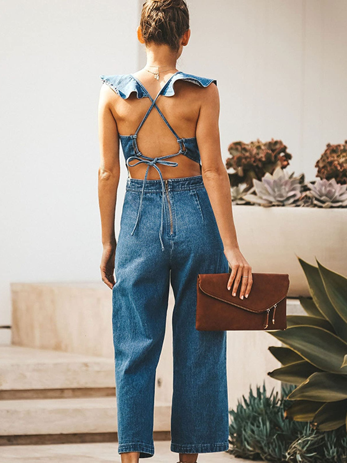 Ruffled denim jumpsuit with crossover back straps and tie detail.