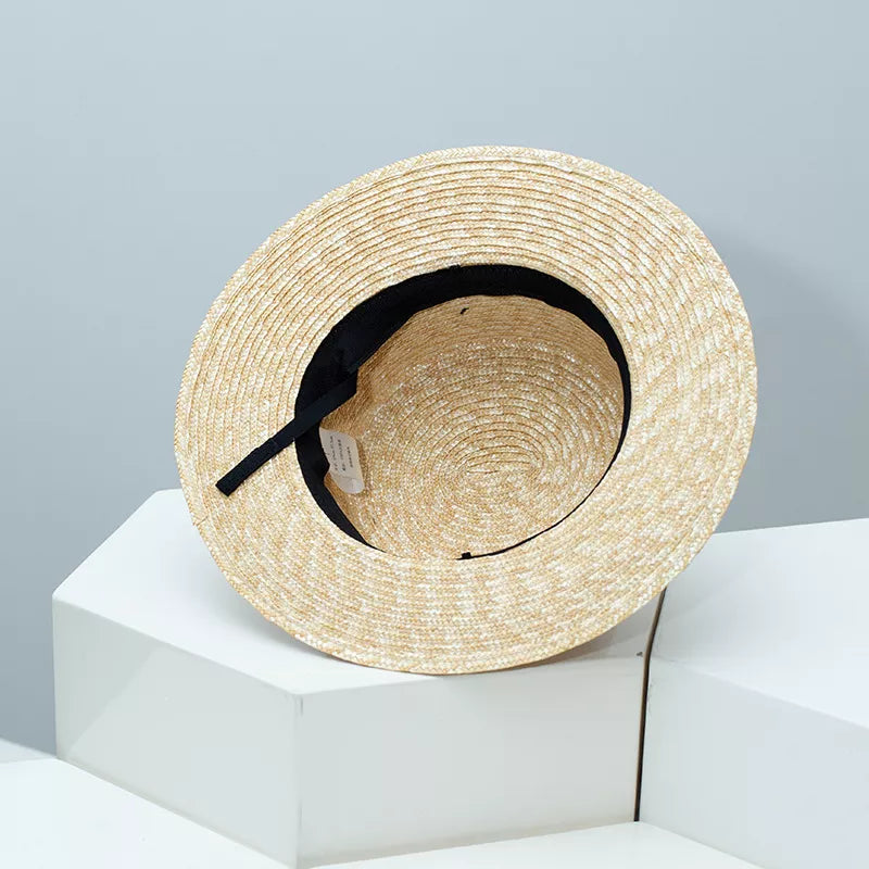 Elegant straw boater hat in tan with black ribbon trim, showing interior detail.